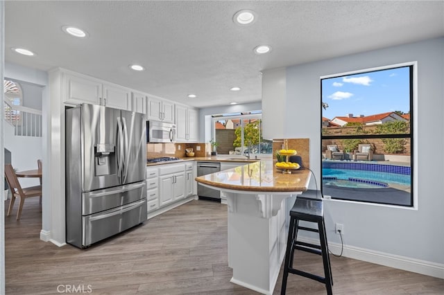 kitchen featuring light wood finished floors, a breakfast bar, a peninsula, white cabinets, and appliances with stainless steel finishes