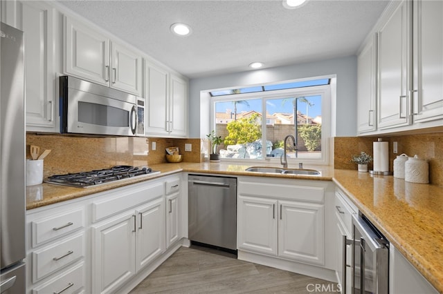 kitchen featuring a sink, backsplash, white cabinetry, stainless steel appliances, and light wood finished floors