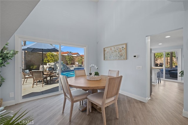 dining room with a towering ceiling, recessed lighting, baseboards, and light wood finished floors