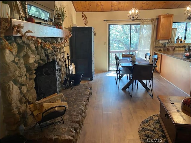 dining room featuring light wood-type flooring, an inviting chandelier, wood ceiling, and a stone fireplace