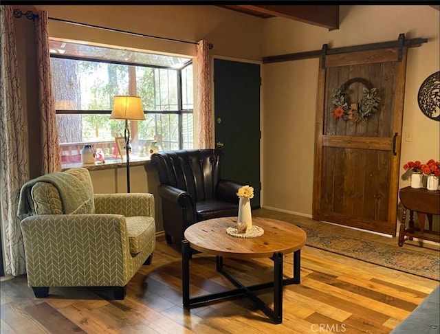 sitting room featuring wood finished floors, beamed ceiling, baseboards, and a barn door