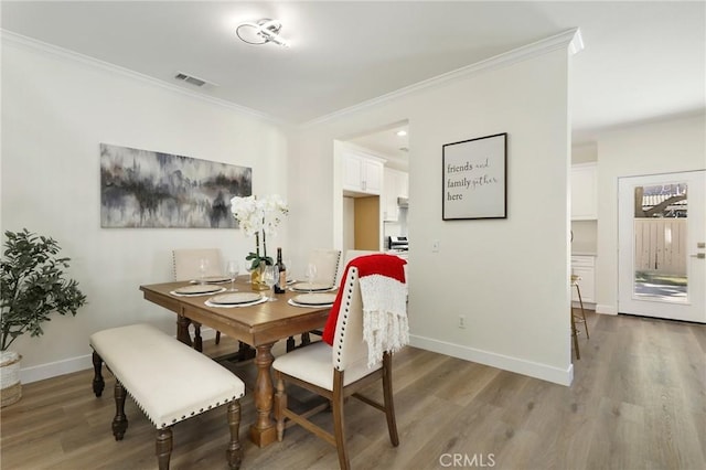 dining space featuring ornamental molding, visible vents, light wood-style floors, and baseboards