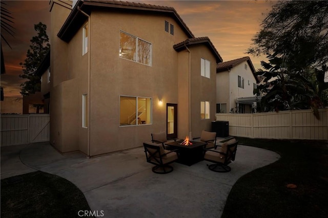 back of property at dusk with a fire pit, a patio, fence, and stucco siding