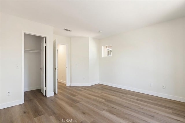 unfurnished bedroom with visible vents, baseboards, wood finished floors, a walk in closet, and a closet