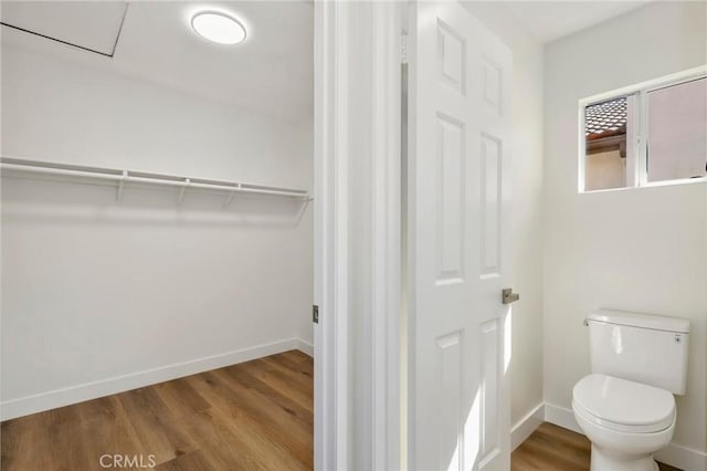 bathroom with toilet, a spacious closet, baseboards, and wood finished floors