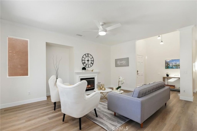 living area with light wood-style floors, a glass covered fireplace, visible vents, and baseboards