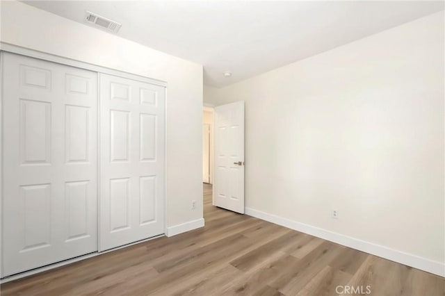 unfurnished bedroom with a closet, wood finished floors, visible vents, and baseboards