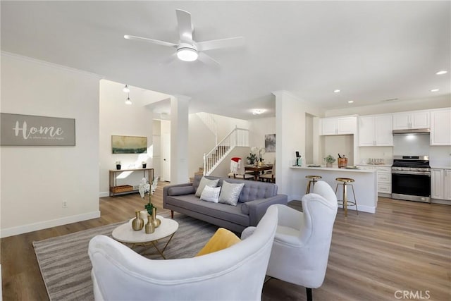 living area with recessed lighting, ornamental molding, wood finished floors, baseboards, and stairs