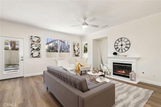 living room featuring baseboards, visible vents, a glass covered fireplace, ornamental molding, and wood finished floors