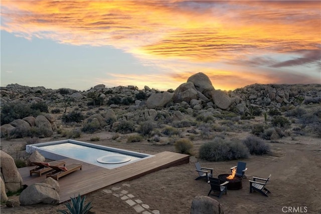 pool at dusk with an outdoor fire pit and a wooden deck