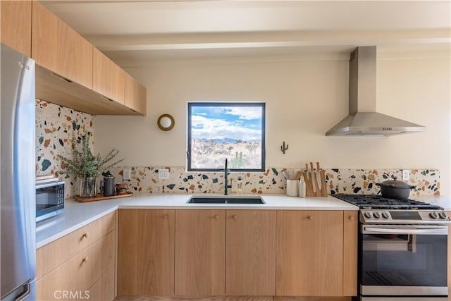 kitchen featuring light brown cabinetry, wall chimney range hood, a sink, and appliances with stainless steel finishes