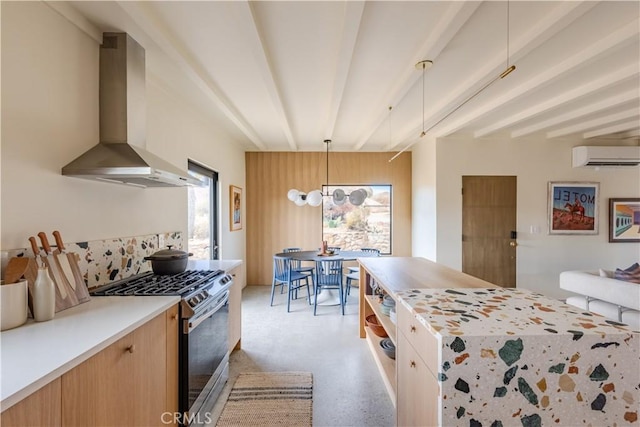 kitchen with light countertops, a wall mounted AC, gas stove, wall chimney range hood, and beamed ceiling