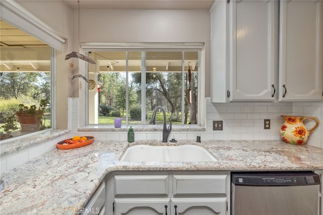 kitchen featuring light stone counters, a sink, white cabinetry, backsplash, and dishwasher