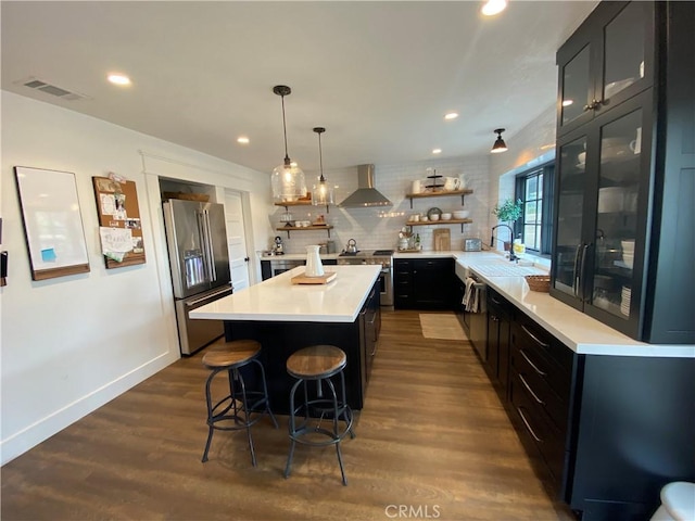 kitchen featuring light countertops, high quality fridge, dark cabinetry, wall chimney exhaust hood, and open shelves