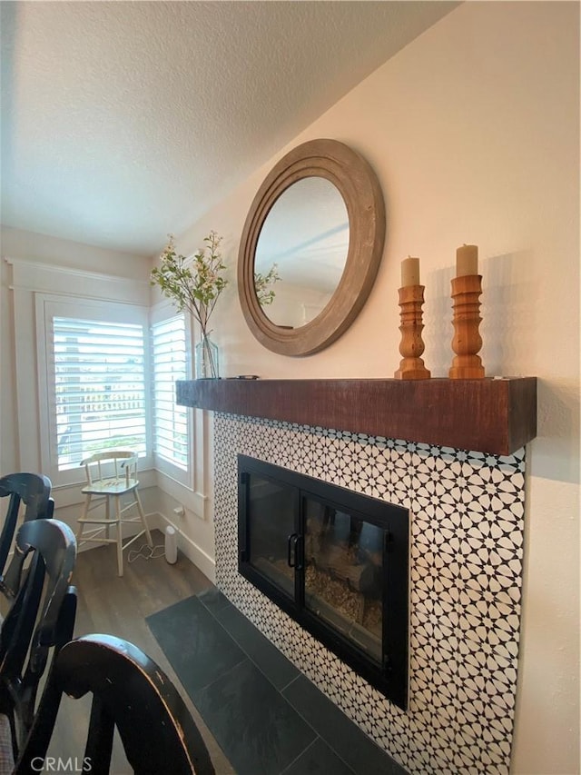 interior details with a tile fireplace, a textured ceiling, baseboards, and wood finished floors