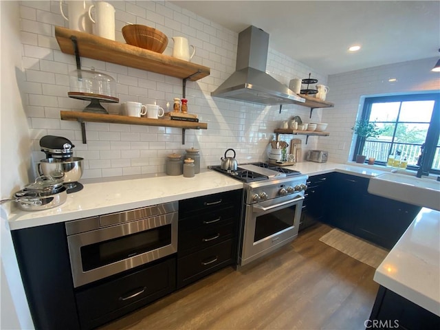 kitchen with dark wood-style floors, open shelves, stainless steel appliances, wall chimney range hood, and dark cabinets