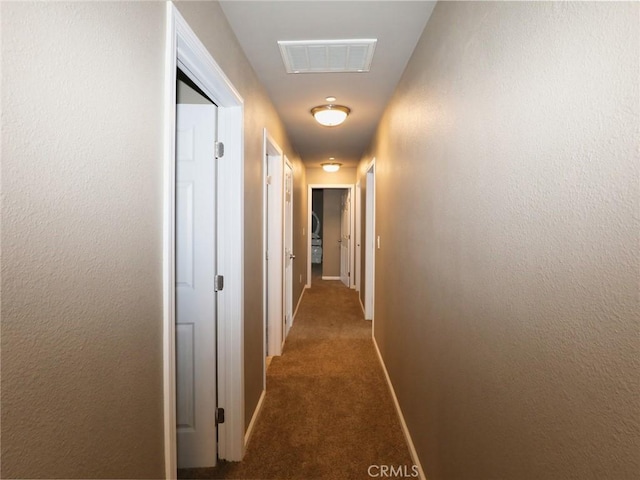 corridor featuring a textured wall, baseboards, visible vents, and carpet floors