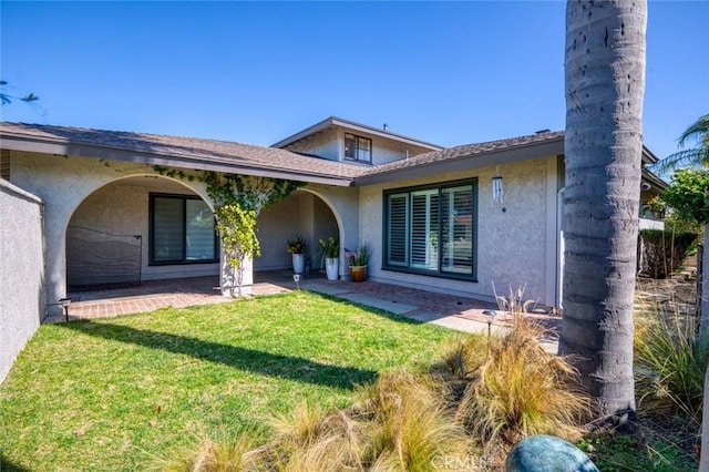 rear view of house with a lawn and stucco siding