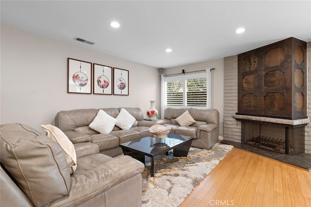 living area with light wood-type flooring, a brick fireplace, visible vents, and recessed lighting