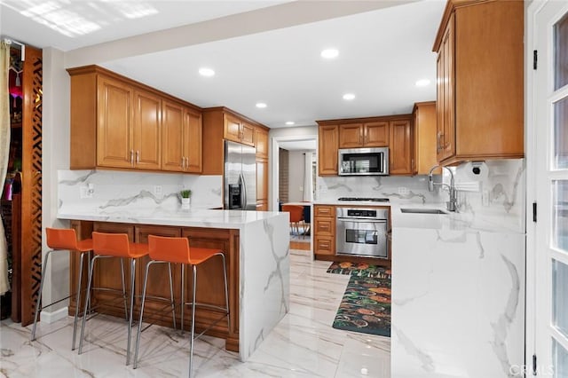 kitchen featuring appliances with stainless steel finishes, brown cabinetry, a sink, and a peninsula