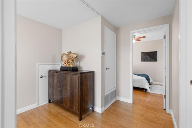 hall featuring light wood-type flooring, visible vents, and baseboards