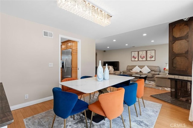 dining space featuring light wood-style floors, a chandelier, visible vents, and baseboards