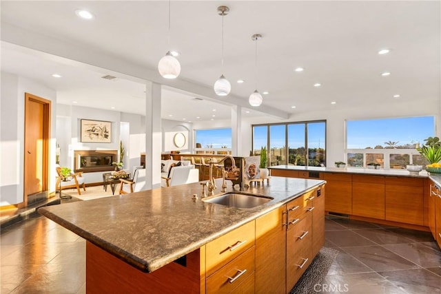 kitchen featuring a glass covered fireplace, open floor plan, a kitchen island with sink, a sink, and recessed lighting