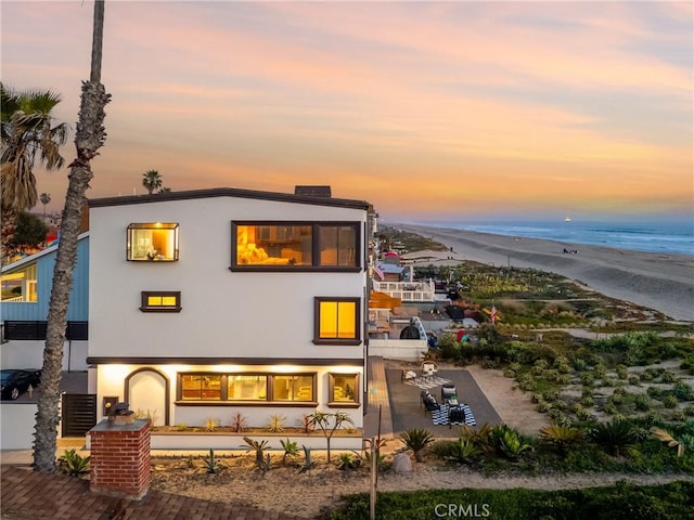 rear view of property featuring a water view, a beach view, and stucco siding