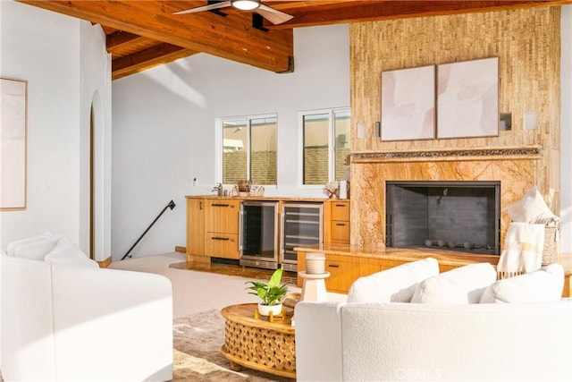 living room with lofted ceiling with beams, ceiling fan, wine cooler, and a high end fireplace