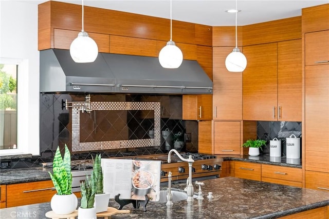 kitchen featuring brown cabinets, decorative backsplash, decorative light fixtures, and under cabinet range hood