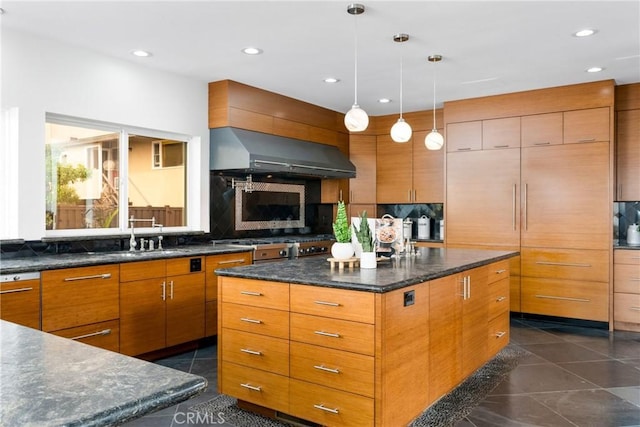 kitchen with a kitchen island, exhaust hood, brown cabinetry, and stainless steel gas stovetop