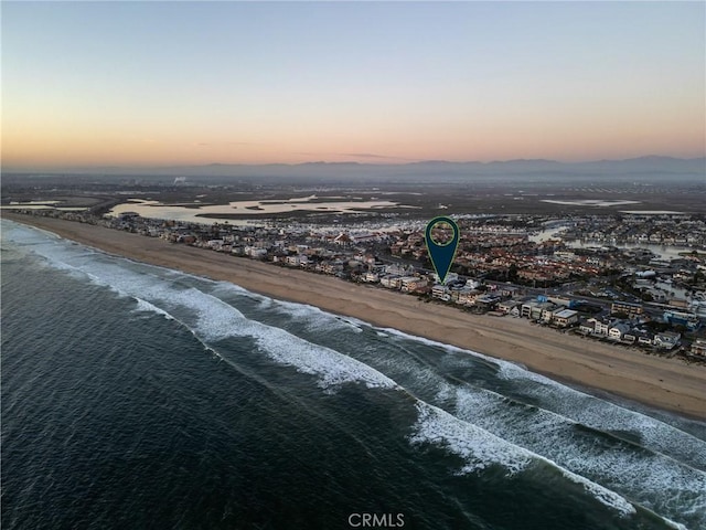 aerial view at dusk featuring a water view and a beach view