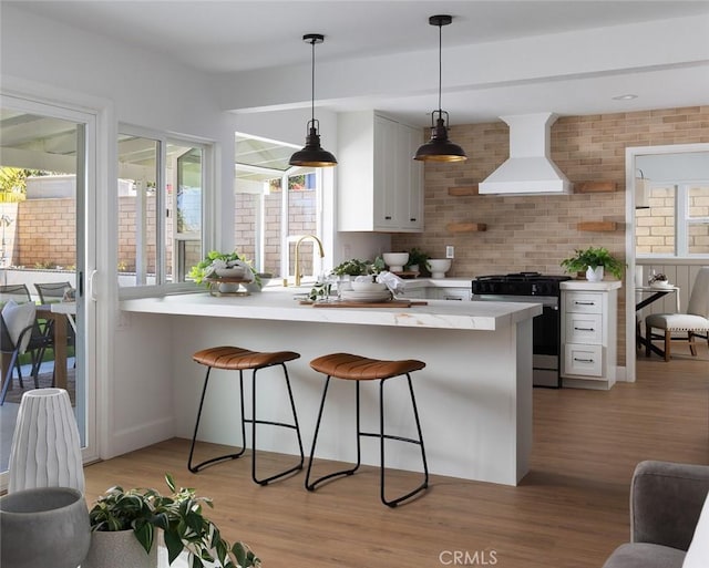 kitchen with wall chimney range hood, light countertops, light wood-style floors, a kitchen breakfast bar, and stainless steel gas stove