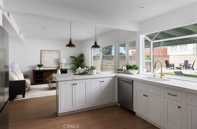 kitchen with dark wood finished floors, light countertops, a peninsula, stainless steel dishwasher, and a sink