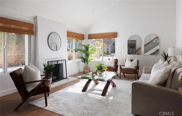 living area with high vaulted ceiling, a fireplace with raised hearth, wood finished floors, baseboards, and stairs