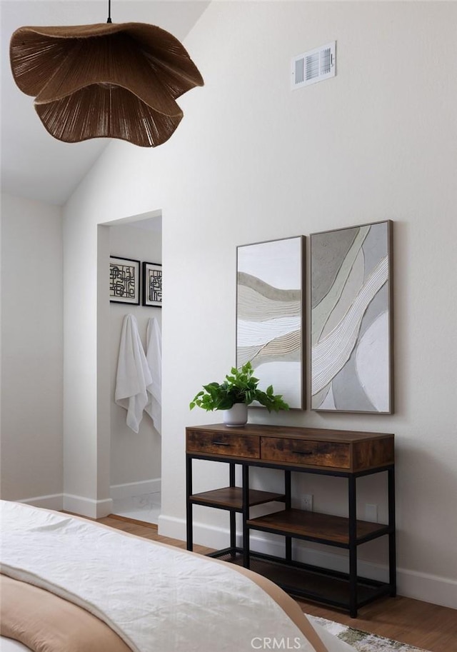 bedroom with vaulted ceiling, wood finished floors, visible vents, and baseboards