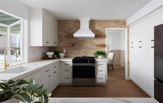 kitchen featuring stainless steel gas range oven, a sink, white cabinets, wall chimney exhaust hood, and dark wood-style flooring