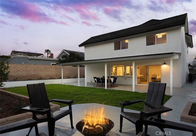 rear view of house with a fire pit, fence, stucco siding, a yard, and a patio