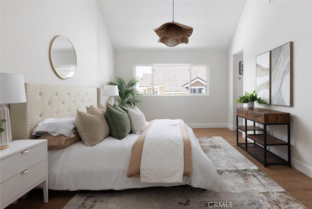 bedroom with baseboards, lofted ceiling, and wood finished floors