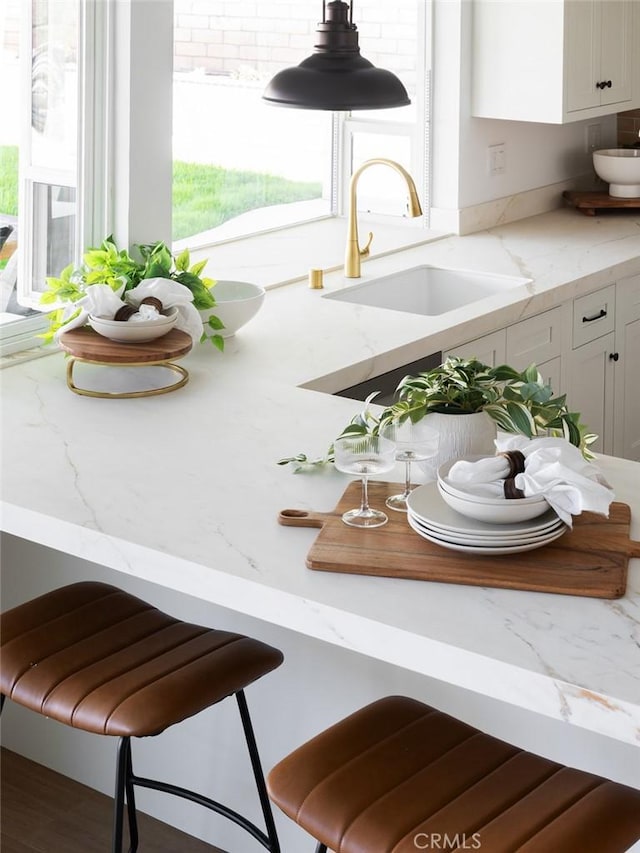 kitchen featuring a sink, light stone counters, and white cabinetry