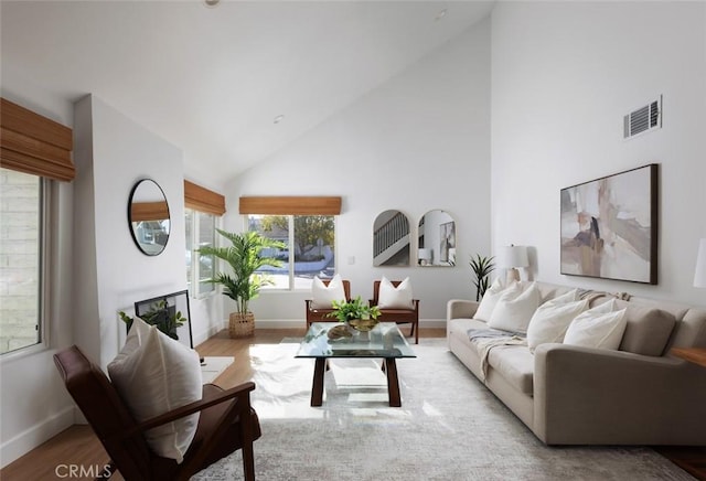 living area with visible vents, high vaulted ceiling, light wood-type flooring, and baseboards