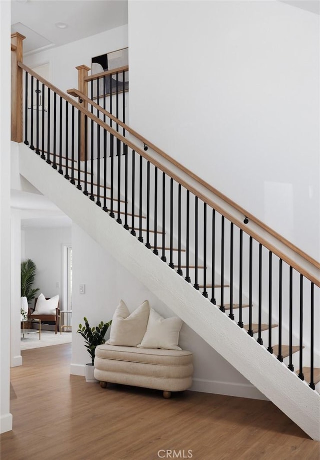 stairway featuring baseboards, a high ceiling, and wood finished floors