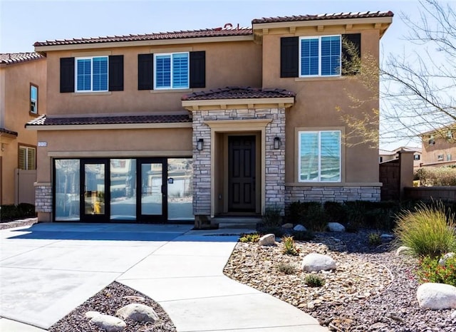 view of front facade featuring stone siding, concrete driveway, a tiled roof, and stucco siding