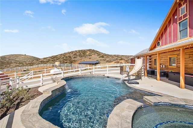 view of swimming pool featuring an in ground hot tub, a water slide, a mountain view, and a patio