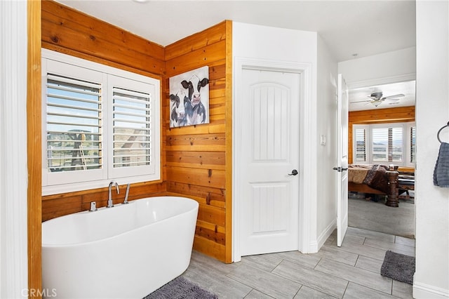 ensuite bathroom featuring a freestanding tub, ceiling fan, wood walls, and ensuite bathroom