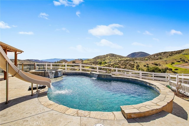 view of swimming pool with a pool with connected hot tub, a patio area, fence, and a mountain view