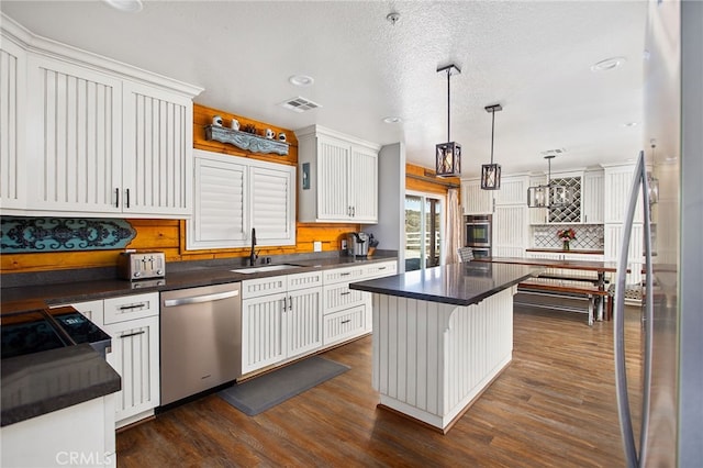 kitchen with a sink, visible vents, stainless steel dishwasher, a center island, and dark countertops