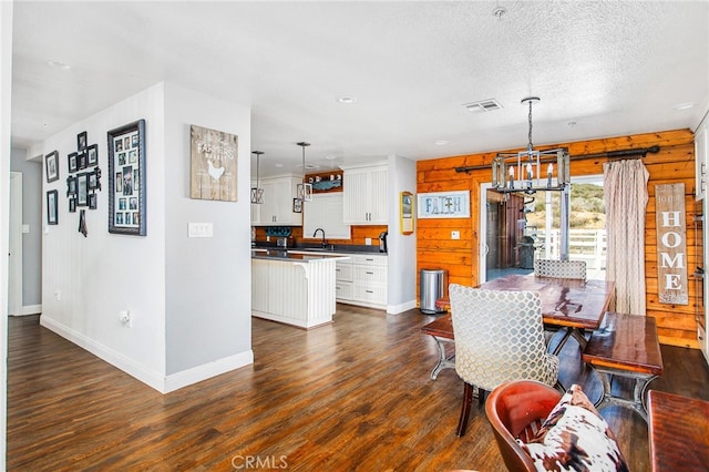 dining room with a textured ceiling, a notable chandelier, visible vents, baseboards, and dark wood-style floors