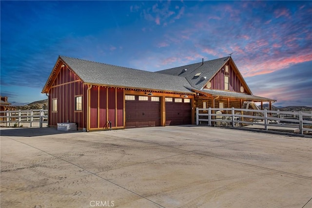 view of side of home featuring a garage, a shingled roof, board and batten siding, and fence