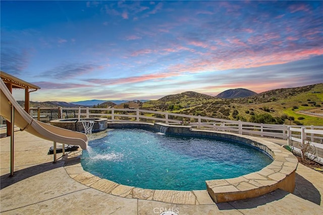 view of pool featuring a pool with connected hot tub, a patio area, a mountain view, and fence